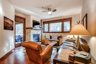 A living room with a fireplace, a large TV, a couch, and two chairs.