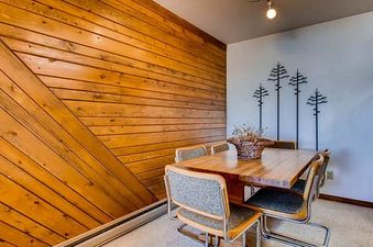 A cozy dining area at Buttes 2 Peak 517 with a large wooden table and chairs, set against a wooden accent wall and a white wall decorated with metal pine tree art.