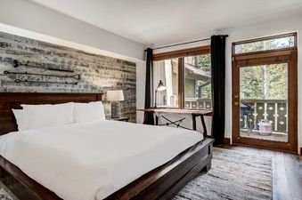 The bedroom in the Arrowhead Village Condominium Premium 2 Bedroom and Loft has a large bed, a wooden dresser, and a large window overlooking a wooded area.