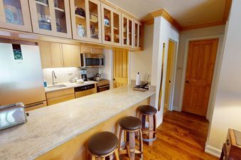 A kitchen with stainless steel appliances and a granite countertop, featuring a toaster, coffee maker, and a small bar with three stools.
