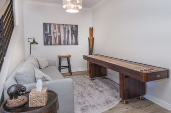 A cozy lounge area featuring a shuffleboard table, a grey sofa, and ski-themed decor, providing a relaxing space at Highlands Slopeside.