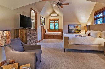 Rustlers Lodge's bedroom features a plush king bed, a separate sitting area with a chair and reading lamp, and a large window that offers an external view.