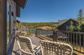 A spacious balcony at Big Horn 43 with two chairs overlooks a serene lake and a dense forest of pine trees under a clear blue sky.