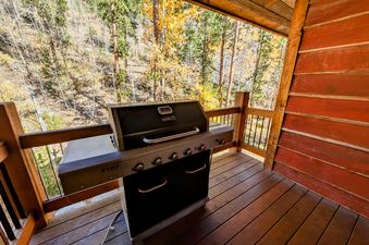 A spacious outdoor deck with a large gas grill and a view of the vibrant autumn forest.