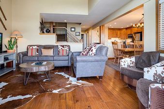 An expansive view of the Ranch at Steamboat RA304's living room and kitchen, featuring a sectional sofa, a tree-slice coffee table, a flat-screen TV, and wooden kitchen cabinetry.