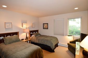 A cozy twin bedroom at 185 Nighthawk Dr features two beds with green comforters, a shared nightstand with a lamp, and a window overlooking lush greenery.