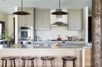 A modern rustic kitchen featuring gray cabinetry, stainless steel appliances, a large island with wooden stools, and unique pendant lighting.