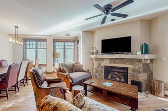 A living room with a fireplace, couch, coffee table, and two large windows