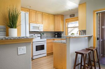 The kitchen of Sawmill Station 217 features light wood cabinets, white appliances, and a breakfast bar with wooden stools.