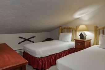 The image features a cozy bedroom in Vantage Point 501 with twin beds, rustic wooden headboards, and a charming birdhouse lamp on a wooden nightstand.