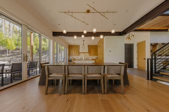 Modern open-plan dining room with a large wooden table, pendant lighting, and scenic mountain views through sliding glass doors.