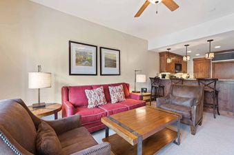 The living room at The Charter C1405 features a red sofa and brown armchairs with a kitchenette in the background.