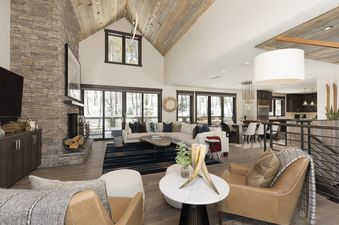 The grand living room at Spanish Peaks Highlands Cabin 36, featuring a stone fireplace, vaulted wooden ceilings, a large sectional sofa, and expansive windows overlooking a snowy landscape.