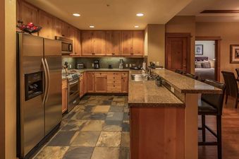 A kitchen with stainless steel appliances, wood cabinets, and a granite countertop. The kitchen is open to a dining area with a table and chairs.