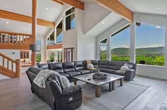 The luxurious living room at Timer Ridge Retreat features a large sectional sofa, a coffee table, and an incredible view of the mountains from the expansive windows.
