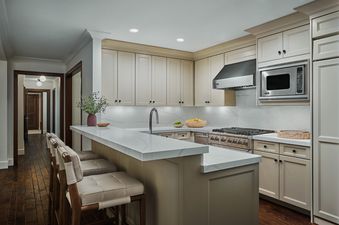 The contemporary kitchen of the Peak View Two Bedroom Residence features light-colored cabinetry, stainless steel appliances, a kitchen island with seating, and a view into the hallway.
