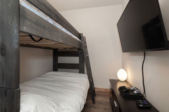 A cozy bunk bedroom at Arrow Stadthaus featuring a wooden bunk bed and a wall-mounted TV with a gaming console.