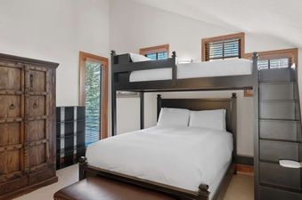 A cozy bunk bedroom at Jay Chalet with a dark wooden bunk bed featuring a full-size lower bed and a twin upper bed, alongside a rustic wooden wardrobe and windows with natural light.
