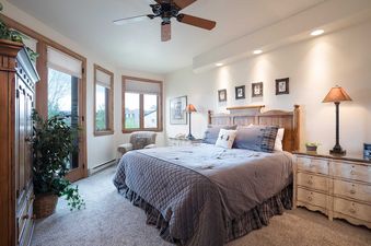The primary bedroom at Chateau Chamonix CX333 features a queen-sized bed with a quilted grey comforter, wooden nightstands with lamps, and large windows with views of the outdoors.