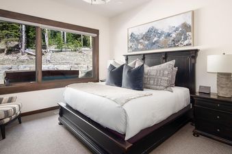 The spacious bedroom of Moonlight Basin 4B Lodgeside features a comfortable king-size bed with a plush duvet, a cozy armchair, and a large window offering views of the surrounding forest.