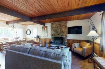 A cozy living room in Cozy Condo on Chamonix Lane featuring a comfortable gray sofa, a stone fireplace, and a dining area visible through an open archway.