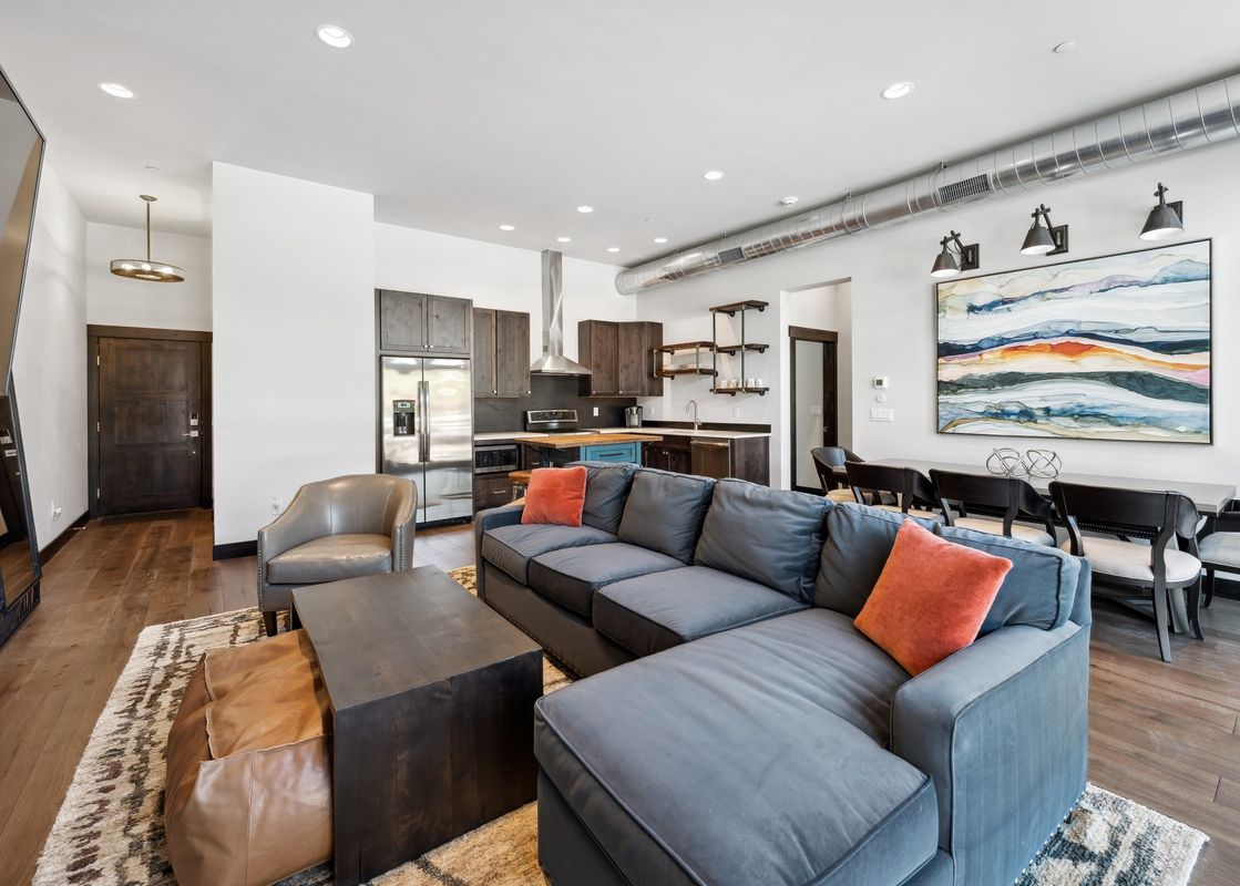 A modern open-concept living space with a gray sectional sofa, a dark wood coffee table, and an integrated kitchen and dining area.