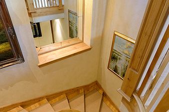 A top-down view of a luxurious spiral staircase at Chill Out, featuring light wood and carpeted treads, with a large arched mirror reflecting the upper floors.