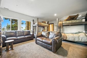 A spacious bunk room with two sets of bunk beds, two brown leather sofas, and large windows offering views of lush greenery.