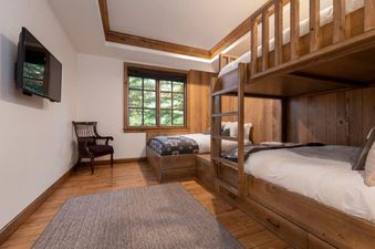 A rustic bunk bedroom at Chateau Beaver Creek Residence 1402 features a wooden bunk bed, a twin bed, a flat-screen TV, and a window with a view of trees.