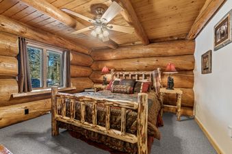 A cozy bedroom with a log bed, rustic decor, and a window overlooking a pine forest in the Stillwater Log Home.