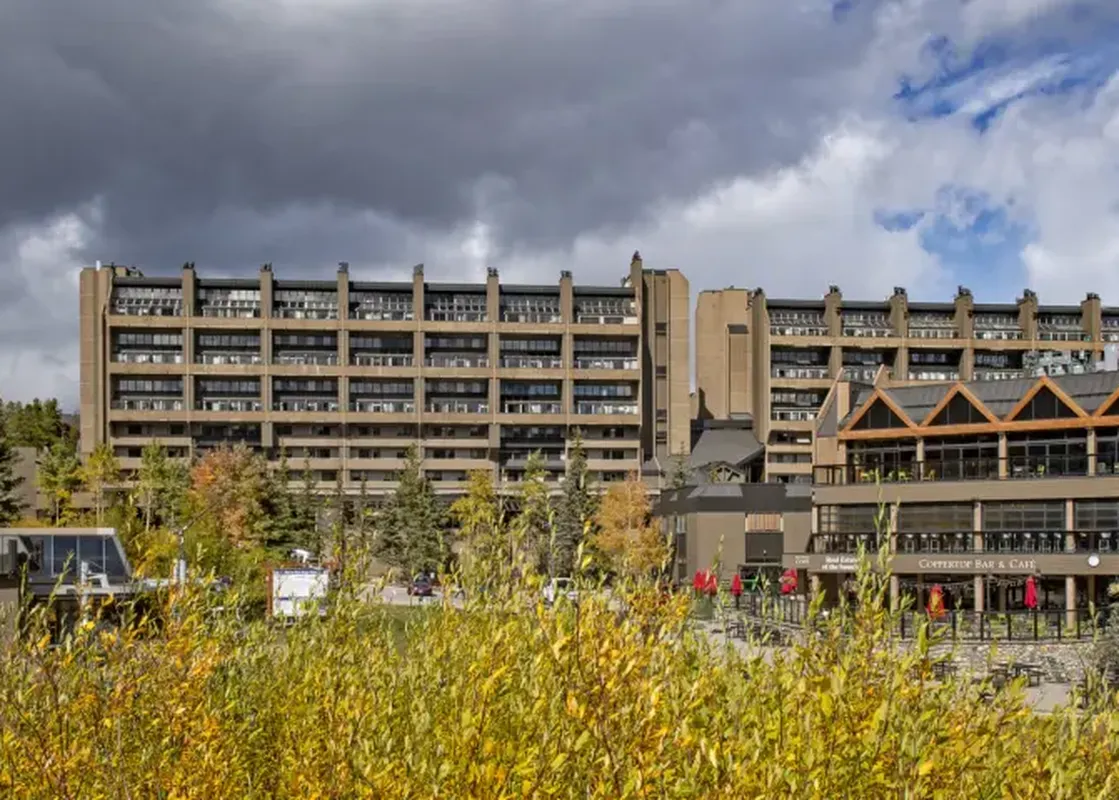 A large multi-story building, One Bedroom Suite Beaver Run Resort, stands amidst colorful autumn trees under a cloudy sky.