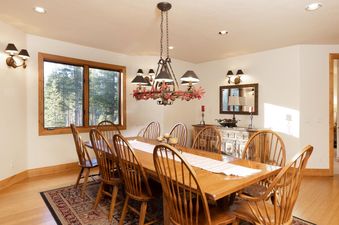 The dining area showcases a large wooden table with nine chairs, set against a backdrop of a window overlooking a forest.
