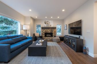 A cozy living room with a fireplace, large windows, a comfy couch, and a TV.
