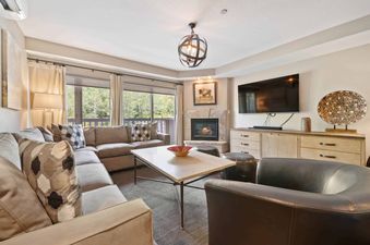 The living area at St James Place 235 features a comfortable sectional sofa, a fireplace, and a large TV, all illuminated by natural light from the windows overlooking the forest.