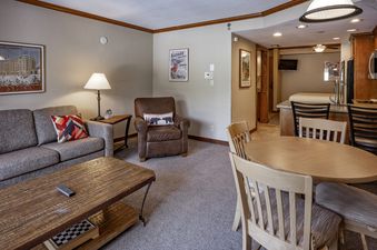 The Breckenridge Studio Beaver Run Resort's studio features a cozy living area with a gray sofa, a leather armchair, a wooden coffee table, a round dining table, and a well-equipped kitchen.