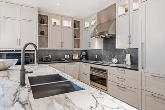 A modern kitchen at Solaris 5F East with light cabinetry, dark marble countertops, a white marble island with a double sink, and stainless steel appliances.