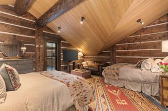 A rustic bedroom with log walls, two beds, and a seating area at Teton Game.