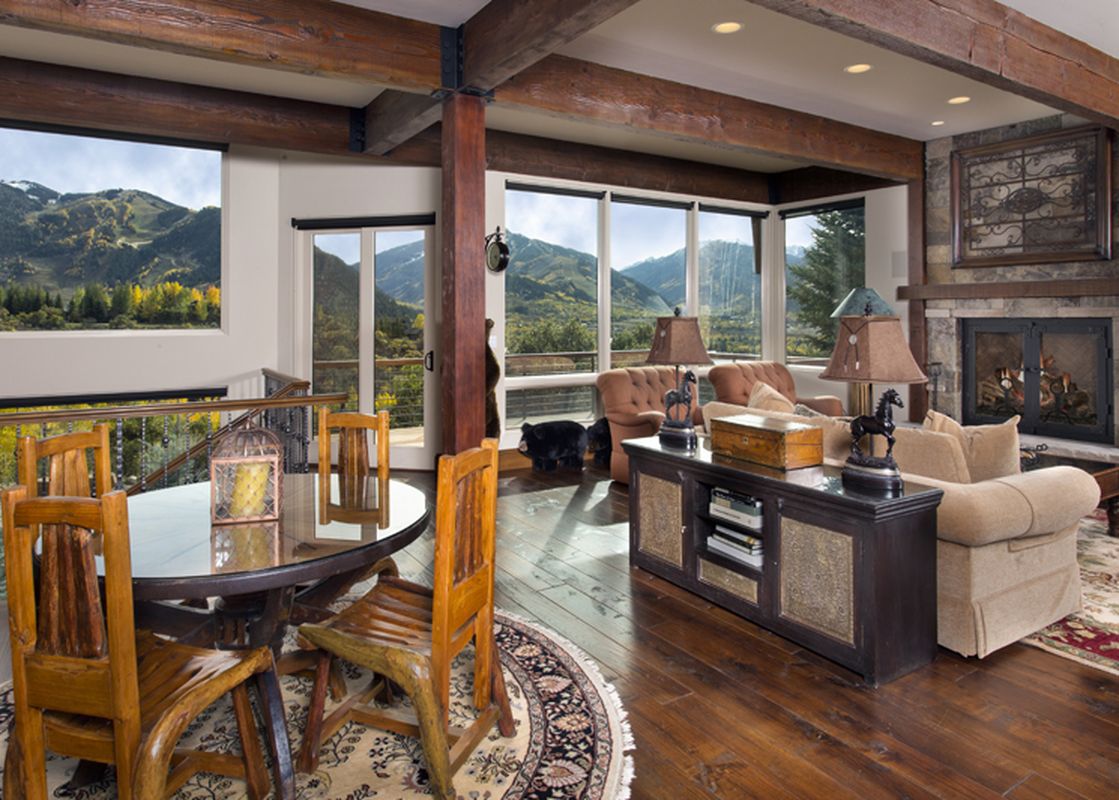 A spacious living area at 185 Nighthawk Dr features wooden beams, a fireplace, and large windows with mountain views, offering both dining and lounging spaces.