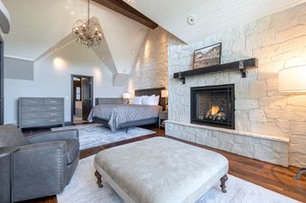 A spacious bedroom with a large bed, a fireplace, and a view of the outdoors from the window