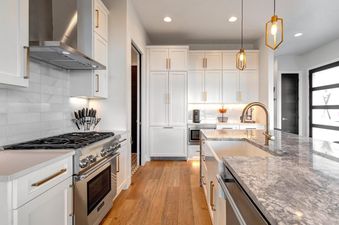 A modern kitchen with white cabinets, stainless steel appliances, and a marble island with an undermount sink.