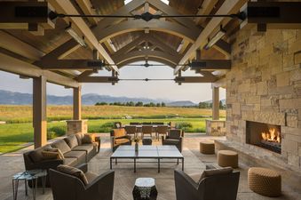 The elegant, covered outdoor pavilion at Le Refuge featuring a large stone fireplace, cozy seating, and sweeping mountain views.