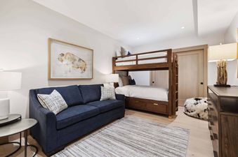 The spacious bedroom at One Riverfront Condo 203 features a cozy blue couch with two pillows, a bunk bed, and an attractive dresser with a unique lamp.