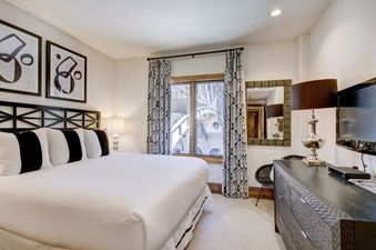 The bedroom at The Arrabelle Two Bedroom features a king-size bed, black and white striped pillows, and dark wood furniture.