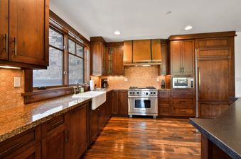 A rustic yet modern kitchen with rich wooden cabinetry, granite countertops, stainless steel appliances, and a farmhouse sink.
