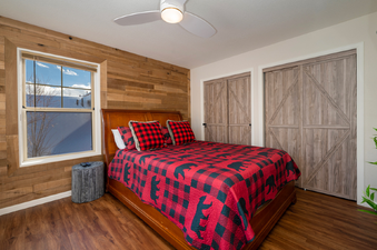 A cozy Waterside West A303 bedroom with rustic wood paneling, a wooden bed frame, and a red and black buffalo plaid comforter with bear silhouettes.