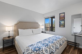 A modern and cozy bedroom in Snowcrest 207 with a queen-size bed, twin nightstands, and a window with an exterior view.