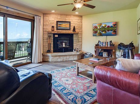 A cozy living room at Ranch at Steamboat RA303 features a stone fireplace, comfortable leather seating, a patterned rug, and sliding glass doors leading to a balcony with mountain views.