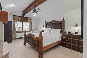 A luxurious bedroom at Silver Strike Lodge 705 features a grand wooden bed, trunk-style nightstands, and a large window overlooking snow-covered mountains, creating a serene and rustic retreat.