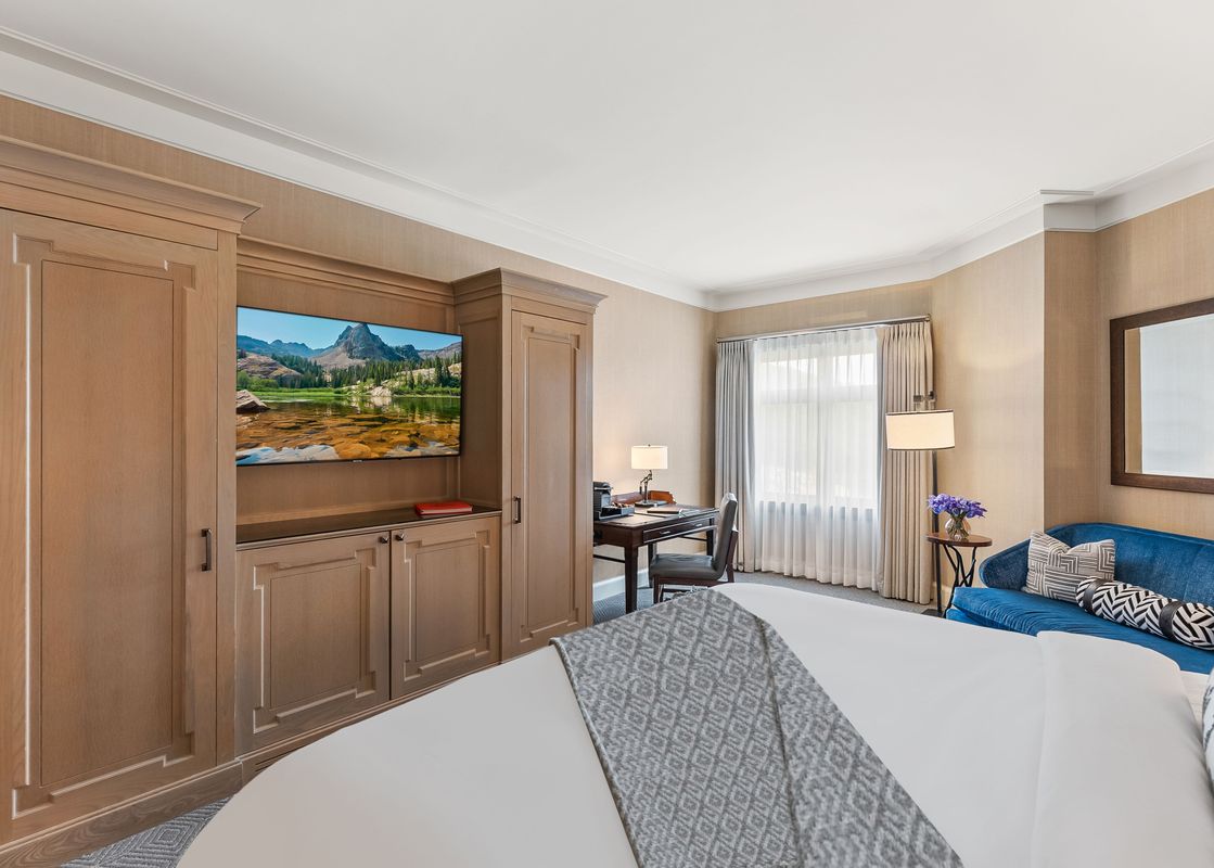 The St. Regis King Room features a comfortable bed, a TV, a desk with a chair, and a blue sofa, creating a luxurious and functional space.