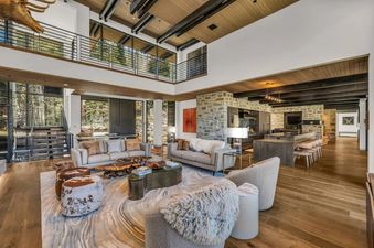 A spacious and luxurious living room at The Foundry, featuring a large seating area, high ceilings with exposed wooden beams, and expansive windows offering views of the outdoors.